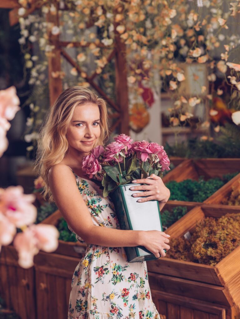 A smiling brand owner holding a bucket of pink roses in her flower pop-up